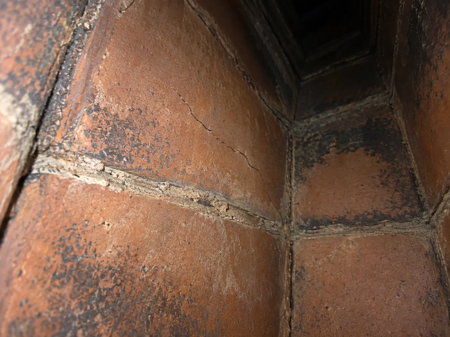 Cracked clay chimney liner with deteriorated mortar joints and soot staining.