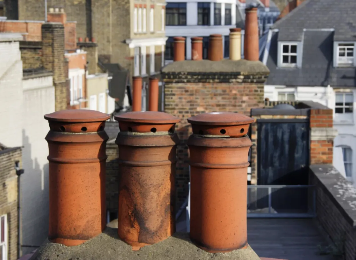 Medium shot of traditional terracotta chimney pots on a mixed-material residential rooftop, showcasing architectural diversity and the importance of flue cleaning and maintenance.